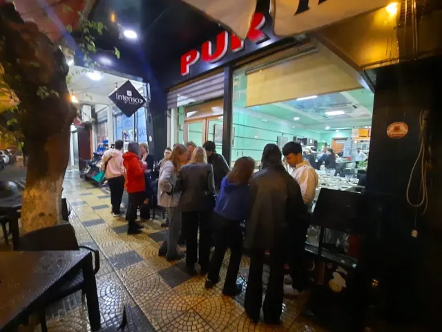 תור אנשים בערב מול דלפק מואר ברחוב, שלט אדום ומדרכה מרוצפת