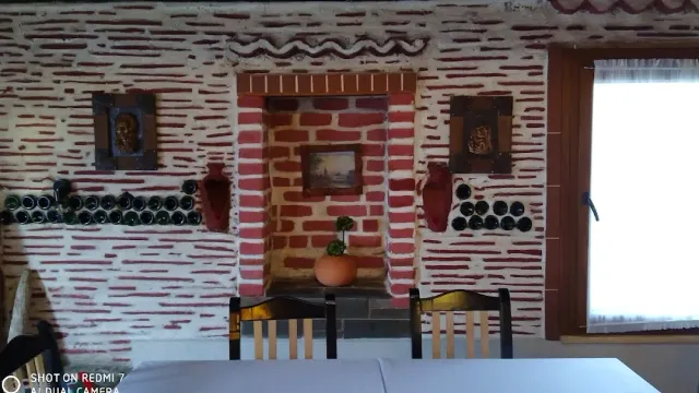 קיר לבנים אדום ולבן עם גומחה, שורות בקבוקים תלויים ושולחן לבן בחזית