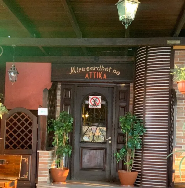 כניסת עץ כהה עם שלט מגולף, פנסים תלויים ועציצים משני צדי הדלת