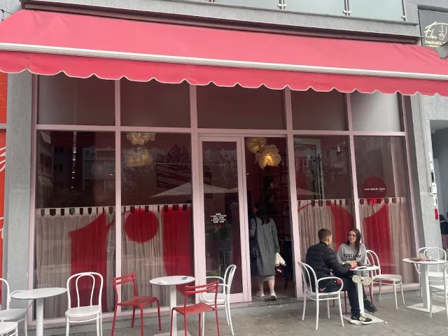 חזית בית קפה עם סוכך אדום, חלונות ראווה וכיסאות לבנים ואדומים על המדרכה
