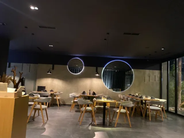 חלל כהה ומעוצב עם מראות עגולות מוארות, שולחנות עץ וכיסאות בהירים