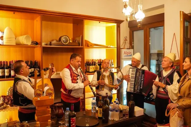 שישה נגנים בתלבושת מסורתית וכובעי לבד לבנים מנגנים באקורדיון ובתוף
