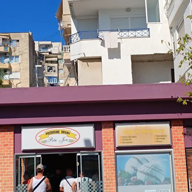 חזית חנות נמוכה עם שני שלטים, לקוחות בכניסה ובנייני מגורים מאחור