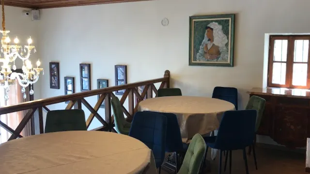 חדר אוכל עם שולחנות עגולים מכוסים מפה, נברשת קריסטל ותמונה ממוסגרת על הקיר