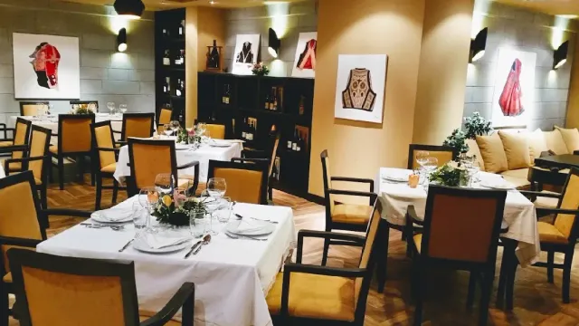 חדר אוכל עם מפות לבנות, כיסאות חרדל ותמונות של תלבושות רקומות על הקירות
