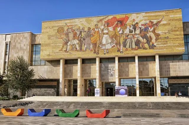 פסיפס ענק של דמויות אוחזות דגל מעל חזית מוזיאון מודרנית ברחבה מרוצפת