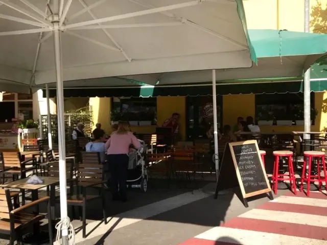ישיבה חיצונית עם שמשיות לבנות, שרפרפים אדומים ולוח תפריט בגיר