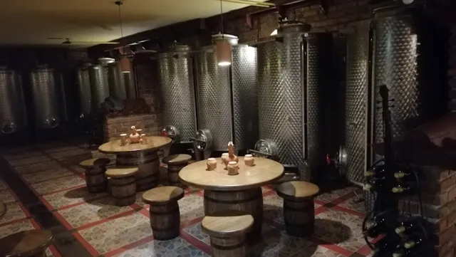 מרתף עם מכלי יין מנירוסטה, שולחנות עגולים וכיסאות חבית עץ