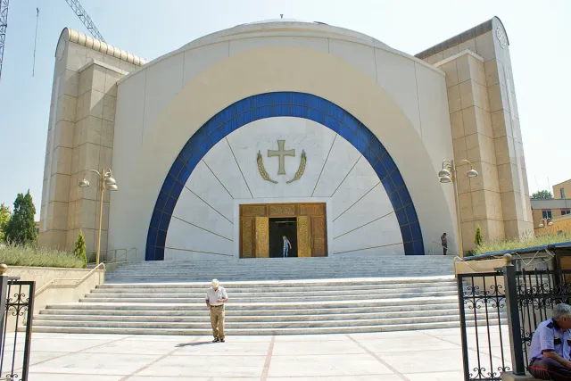 חזית לבנה של קתדרלה מודרנית עם קשת כחולה וצלב מוזהב, מעל מדרגות רחבות