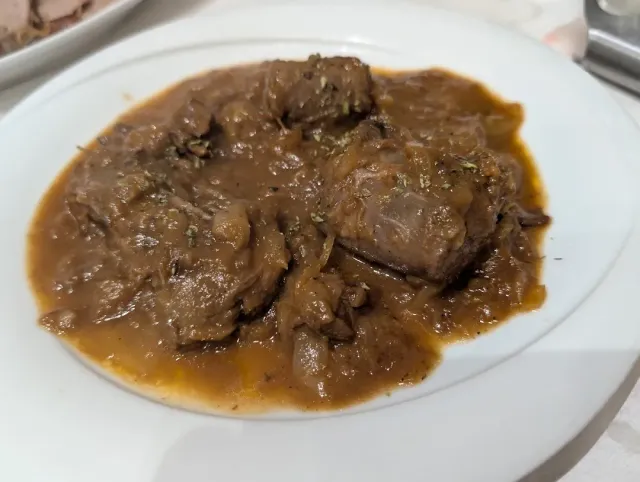 צלחת לבנה עם נתחי בשר ברוטב חום סמיך ובצל מטוגן
