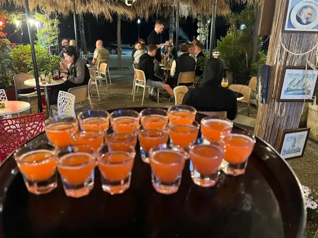 מגש ובו עשרות כוסיות כתומות, ומאחוריו אנשים יושבים בחוץ בלילה