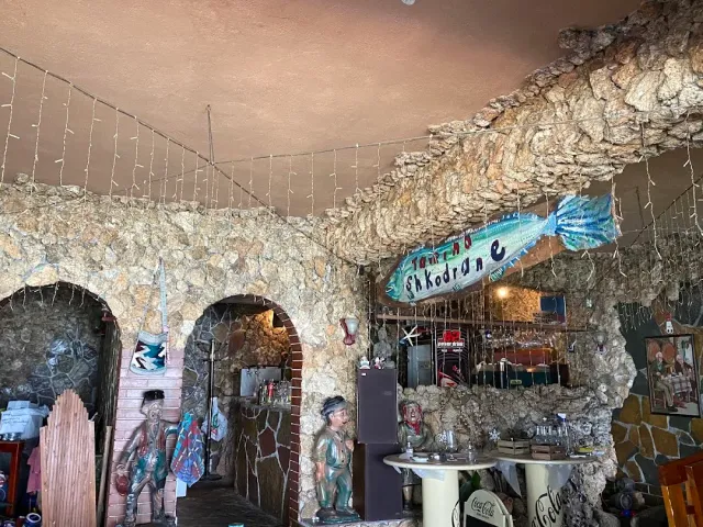 פנים עם קירות אבן גסה וקשתות, שלט בצורת דג ופסלונים על שולחן עגול