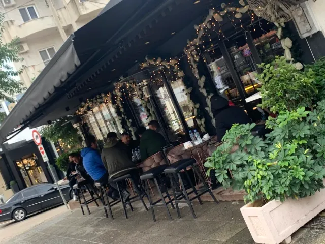 מרפסת רחוב מתחת לסככה שחורה עם נורות חוט ואנשים יושבים על שרפרפים גבוהים