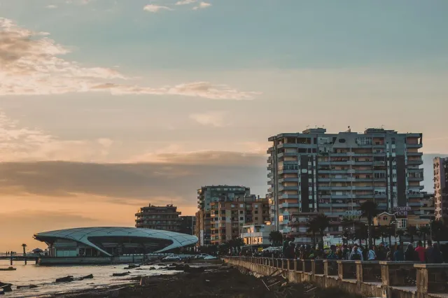 טיילת אבן בשעת דמדומים עם בנייני מגורים גבוהים ומבנה מעוגל על קו המים
