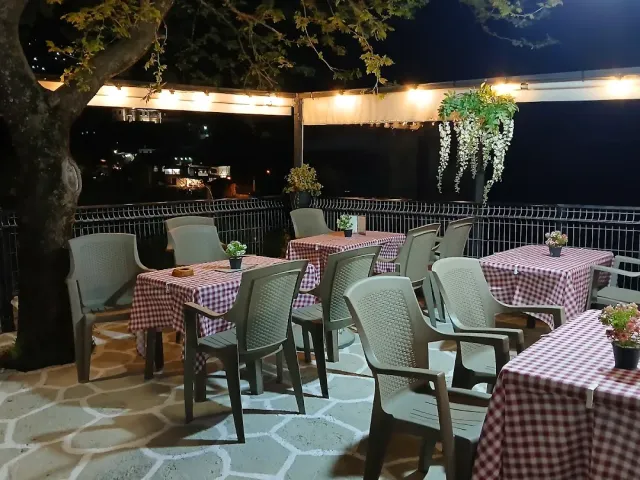 מרפסת בלילה עם מפות משובצות אדום, כיסאות פלסטיק ושרשרת נורות בין העצים