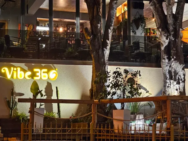 חזית מוארת בלילה עם שילוט צהוב, מפלס עליון מאחורי זכוכית וגדר עץ