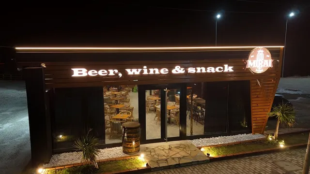 חזית מוארת בלילה עם שלט אור, חלונות זכוכית גדולים וחבית עץ בכניסה