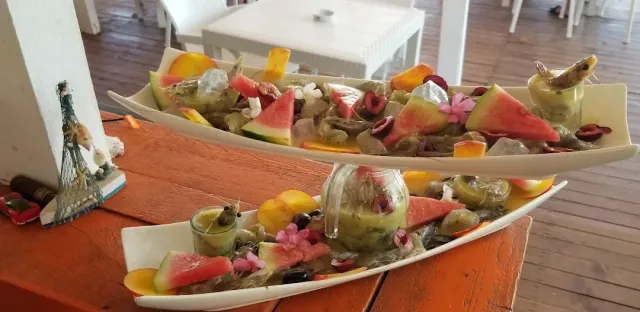 שתי צלחות מוארכות עם פירות ים, משולשי אבטיח, זיתים ופרחים על שולחן כתום