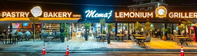 חזית המאפייה בלילה עם השלט המואר ושולחנות על המדרכה