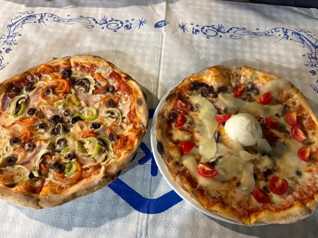 שתי פיצות על מפה לבנה, אחת עם פלפלים וזיתים ואחת עם עגבניות שרי