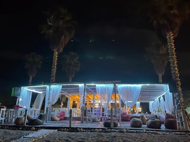 ביתן חוף בלילה עם וילונות לבנים, תאורה כחולה, פופים ודקלים