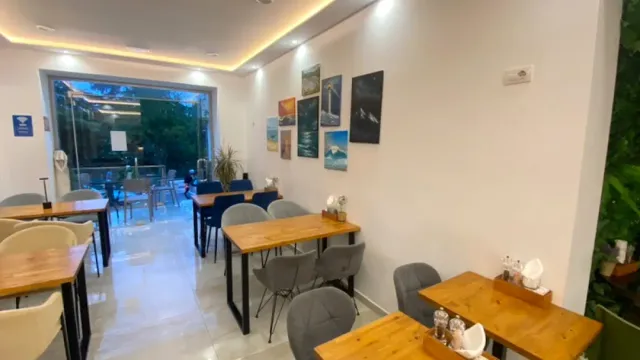 חלל בהיר עם שולחנות עץ, כיסאות אפורים ותמונות ממוסגרות של ים על הקיר