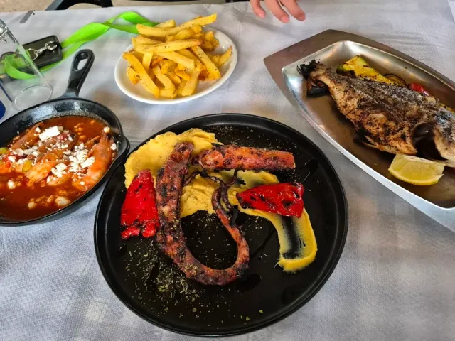 זרוע תמנון על צלחת שחורה עם פלפלים אפויים, לצד צ׳יפס ודג שלם