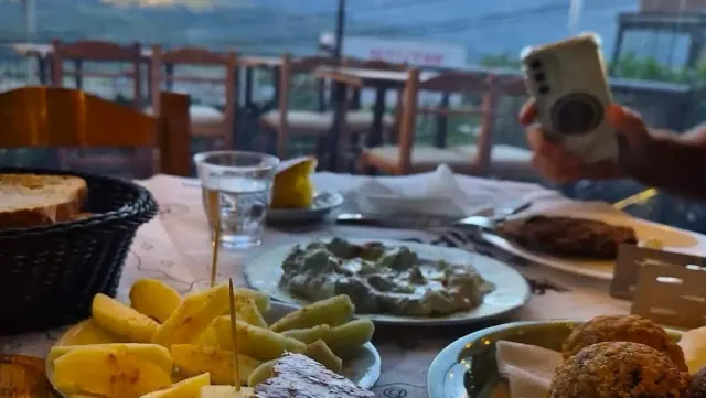 שולחן עמוס מנות עם תפוחי אדמה, מטבל ולחם, ויד המצלמת בטלפון