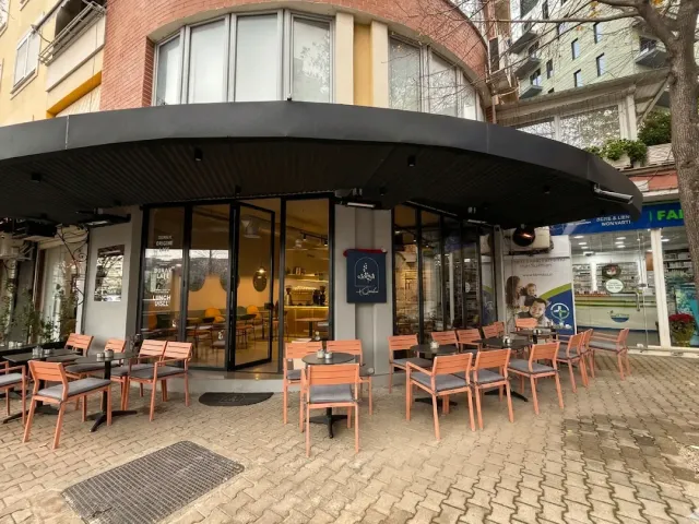 פינת רחוב עם סככה שחורה וכיסאות כתומים על מדרכת אבן מול חזית זכוכית