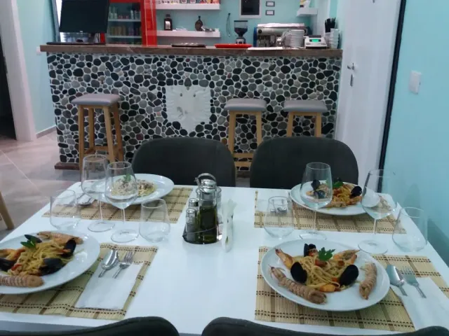 שולחן עם צלחות פסטה ופירות ים, ומאחוריו דלפק מחופה חלוקי נחל