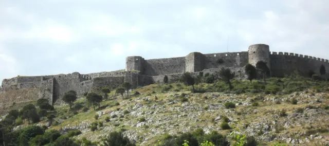 חומות מצודה מאבן על גבעה ירוקה מתחת לשמים מעוננים