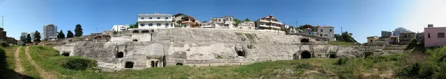 מדרגות אמפיתיאטרון רומי חצובות באבן עם פתחים מקושתים ובתי מגורים מעליהן