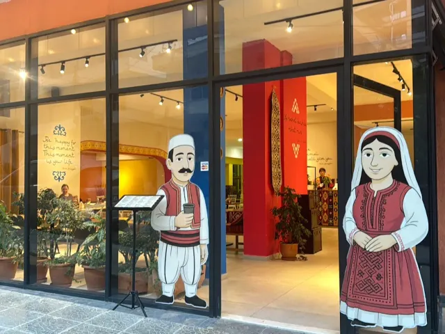חזית זכוכית עם דמויות מצוירות בלבוש מסורתי, פנים צבעוני ועציצים
