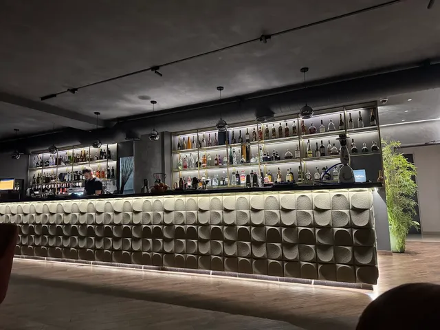 דלפק בר ארוך עם חזית מעוצבת ומדפי בקבוקים מוארים באולם אפלולי