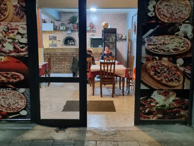 כניסה שמשקופיה מכוסים בתצלומי פיצה גדולים, ומאחוריהם אולם עם תנור לבנים