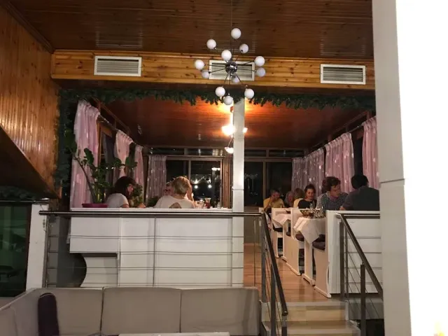 חלל בלילה עם תקרת עץ, נברשת כדורים, וילונות ורודים וסועדים בשולחנות