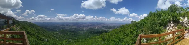 מדרונות יער ירוקים שנפתחים אל מישור העיר הרחוק, תחת שמי קיץ מעוננים