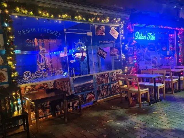 חזית מוארת בכחול עם תצלומי דגים ונורות צבעוניות, וספסלי עץ בחוץ בלילה