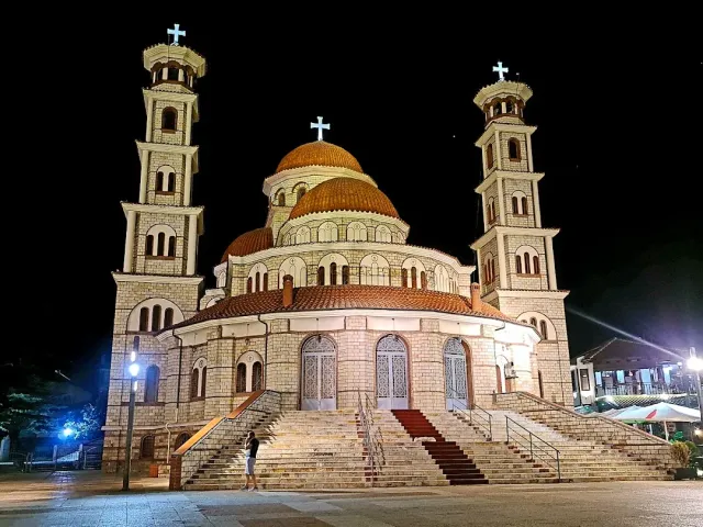 כנסייה מוארת בלילה עם שני מגדלי פעמונים, כיפות אדומות ומדרגות רחבות בכניסה