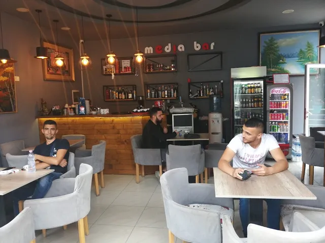 חלל בר עם כורסאות אפורות, מנורות תלויות ומדפי בקבוקים על קיר כהה