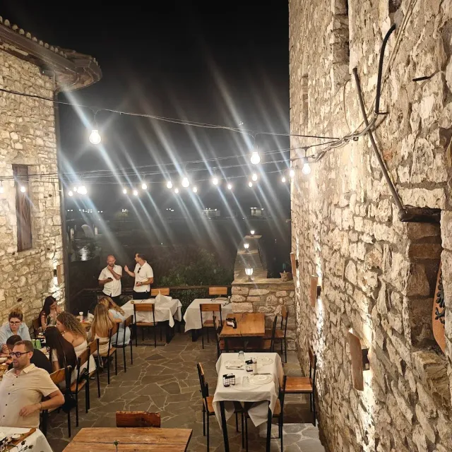 סמטת אבן בלילה עם שרשרת נורות, שולחנות במפות לבנות וסועדים יושבים
