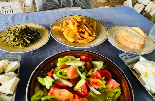 שולחן עם קערת סלט ירקות, צלחת צ׳יפס, עלים מבושלים ופרוסות לחם